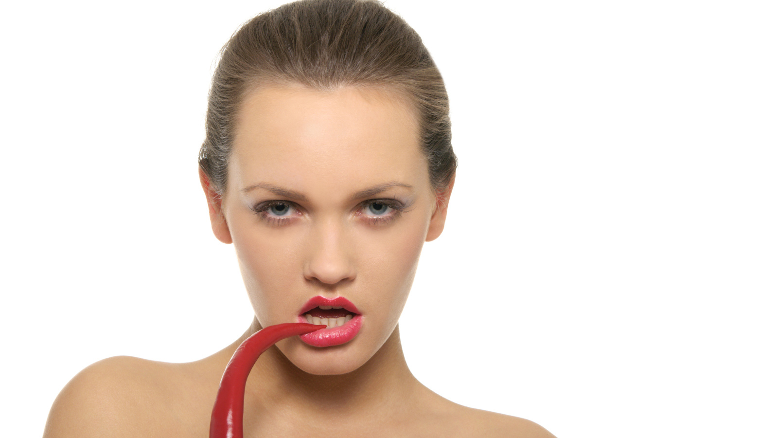 Молодая девушка кусает красный перец на белом фоне