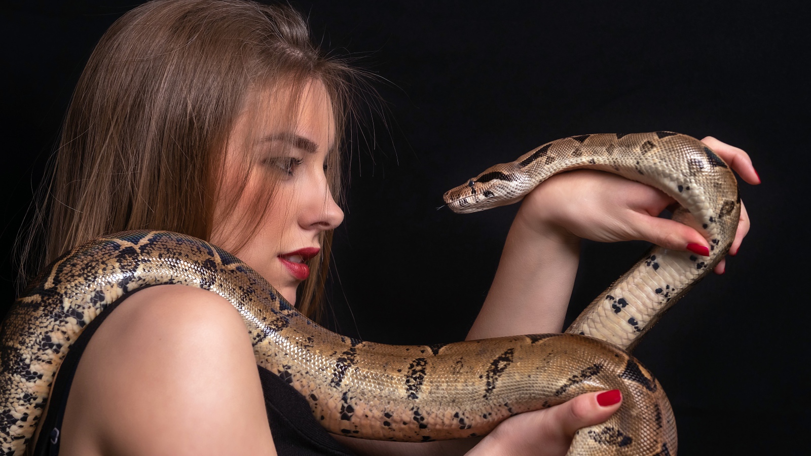 Молодая девушка со змеей в руках на черном фоне
