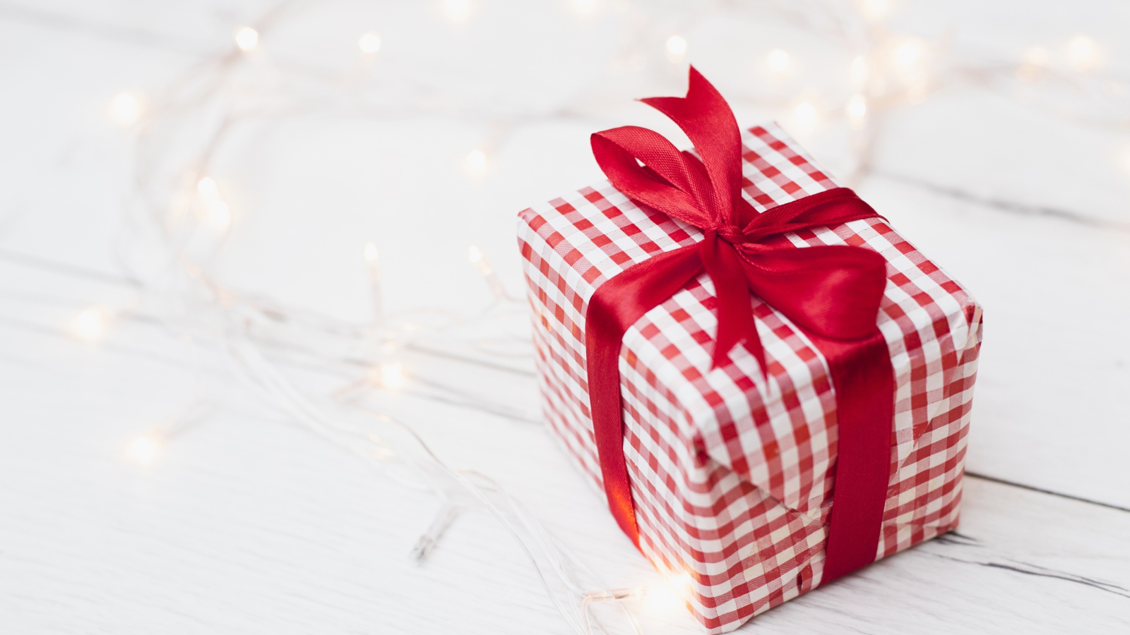 Подарок с красной лентой лежит на столе с гирляндой 