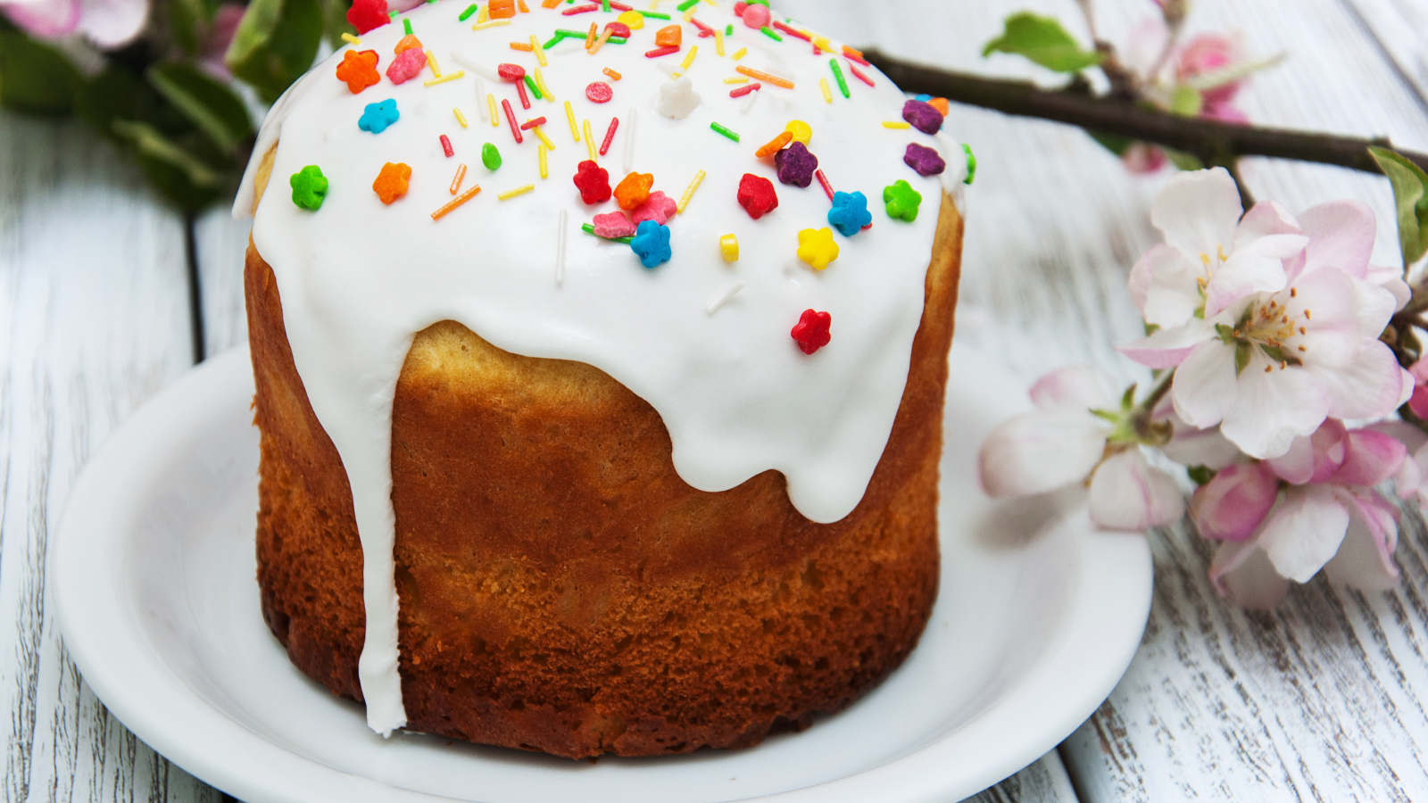 Красивый кулич с белой глазурью на столе с веткой яблони на Великий праздник Пасха