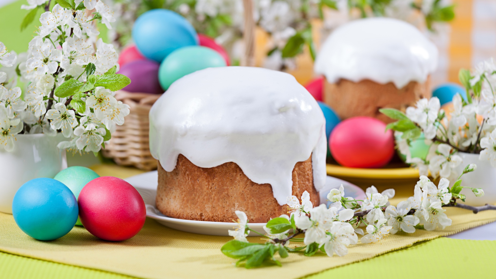 Красивый кулич с белой глазурью на столе с крашеными яйцами и веточками цветущей вишни