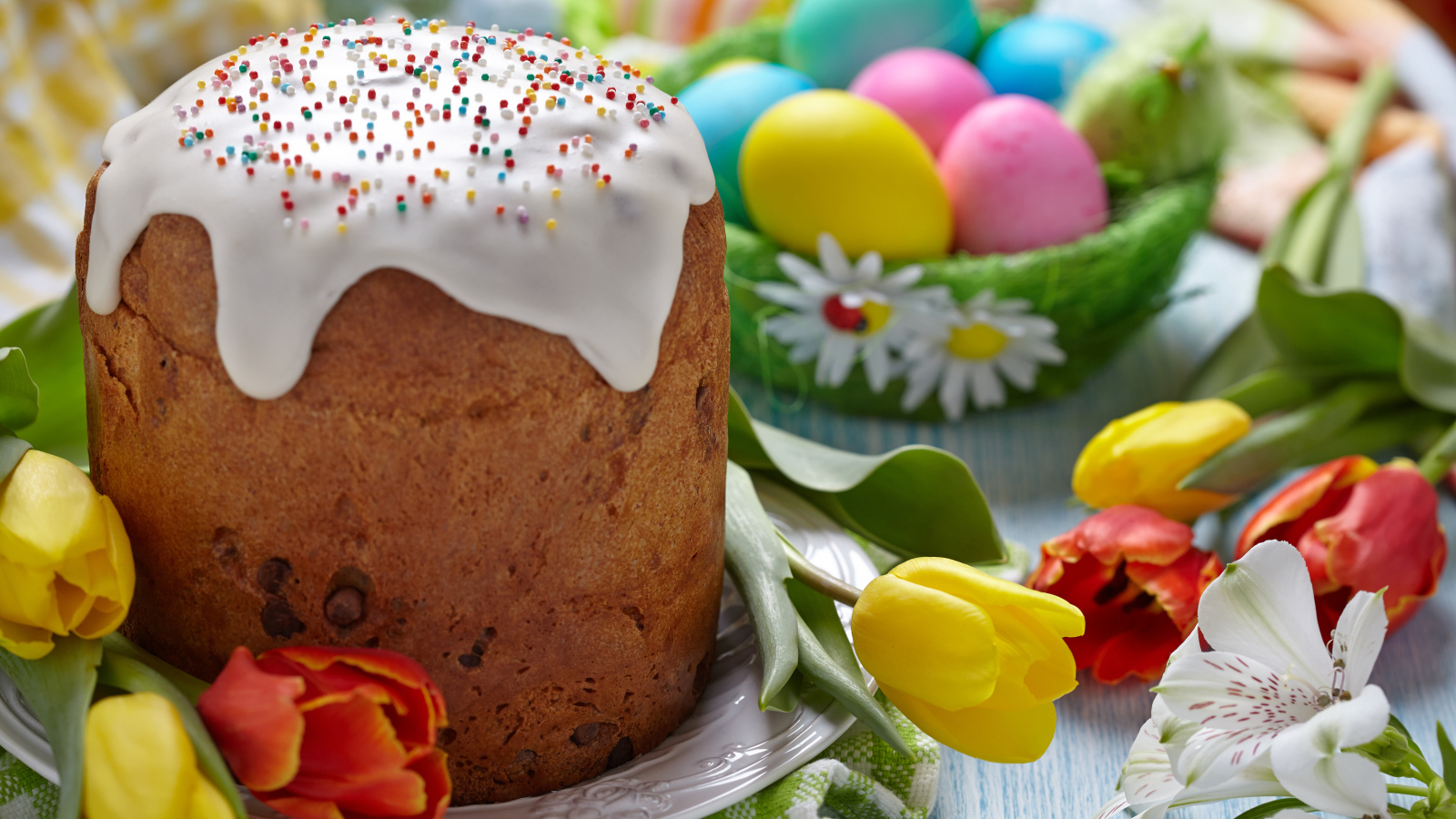 Пасхальный кулич на столе с тюльпанами и крашеными яйцами