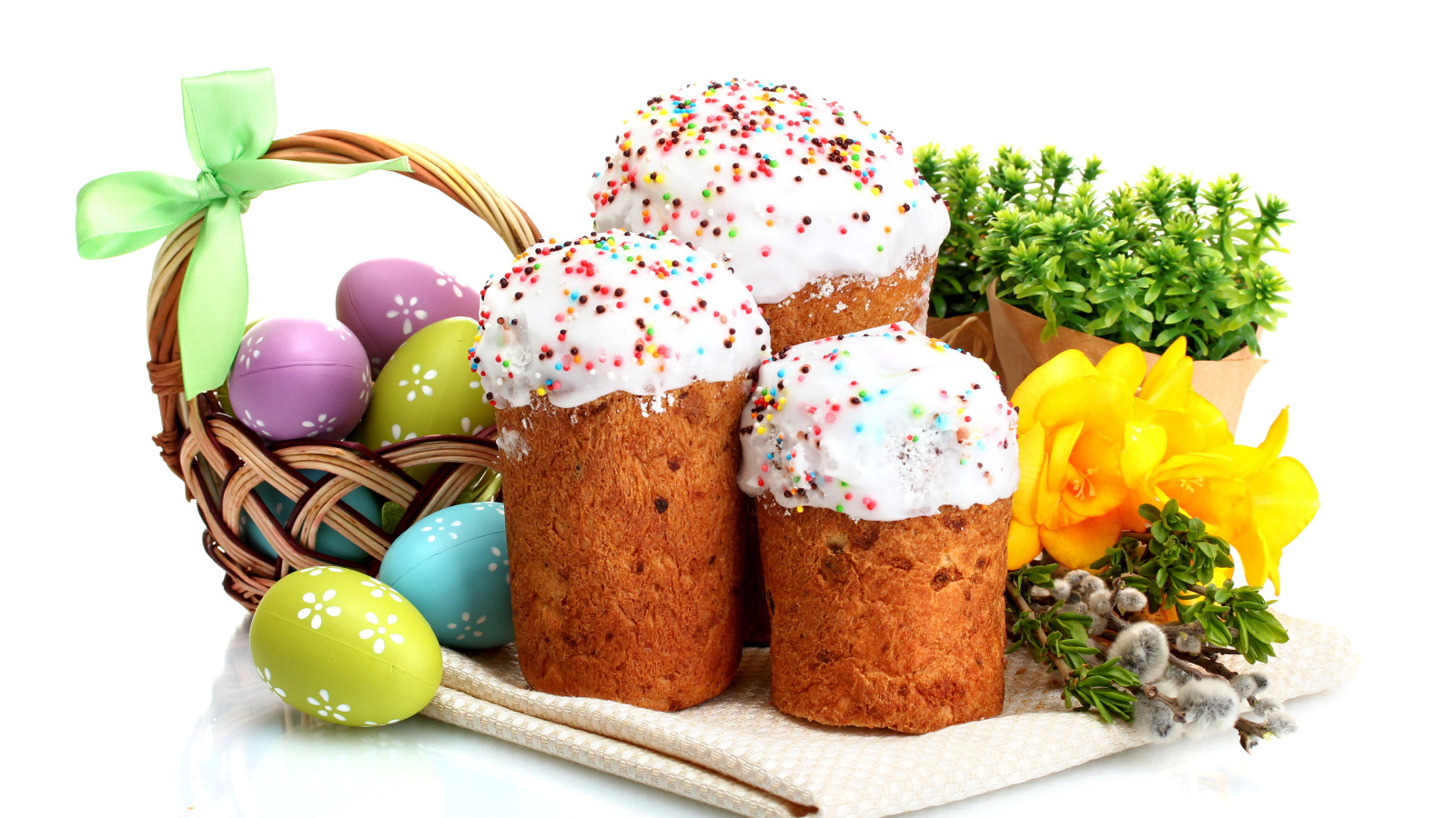 Три сладких кулича на белом фоне с цветами и крашеными яйцами к празднику Пасха