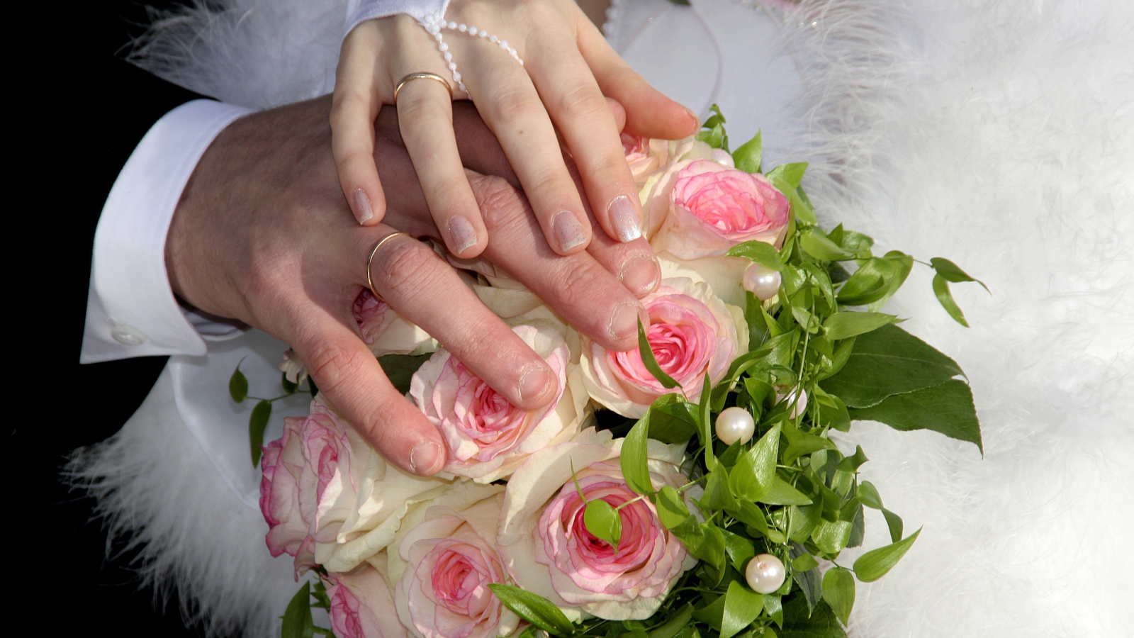 Руки жениха и невесты на букете с розовыми розами