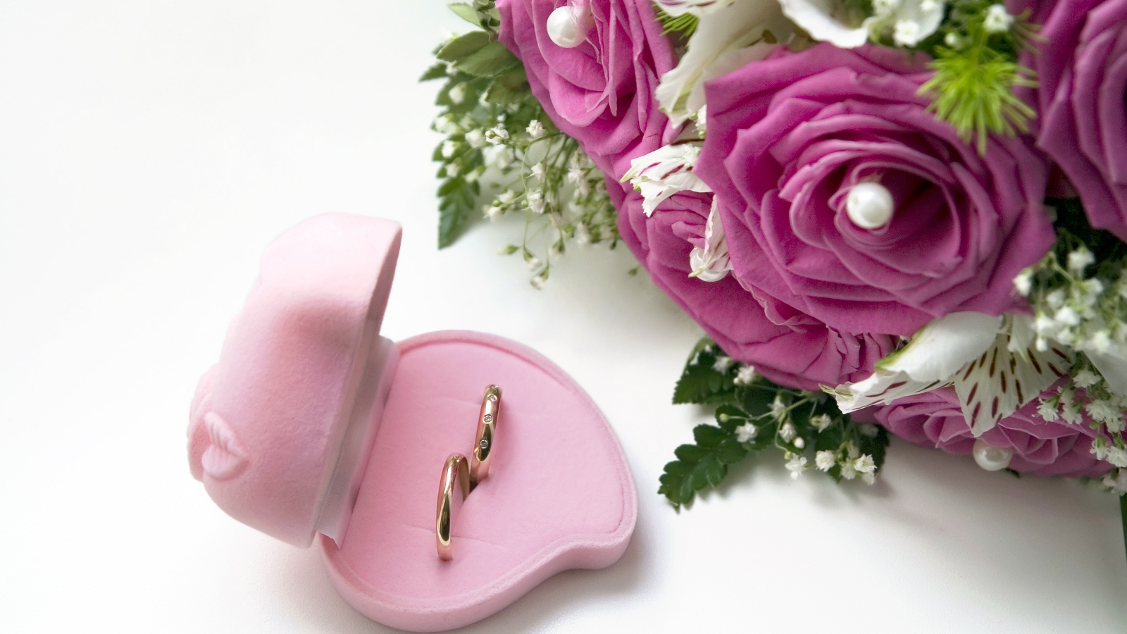 Два обручальных кольца в коробочке на белом фоне с букетом роз