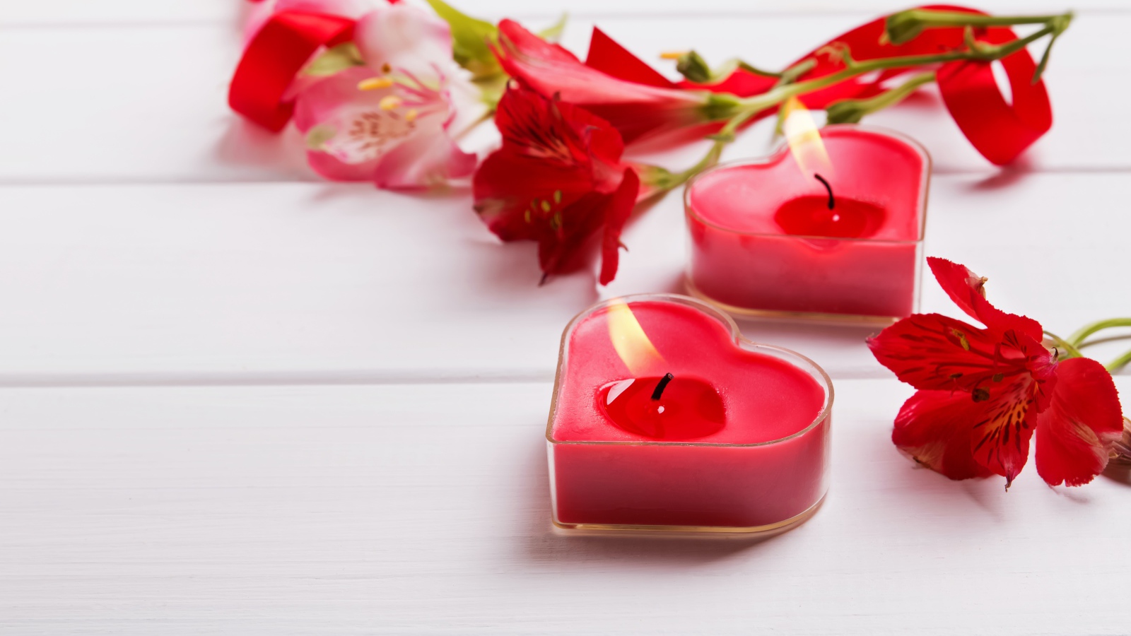 Две красные свечи в форме сердца на столе с цветами альстромерии 