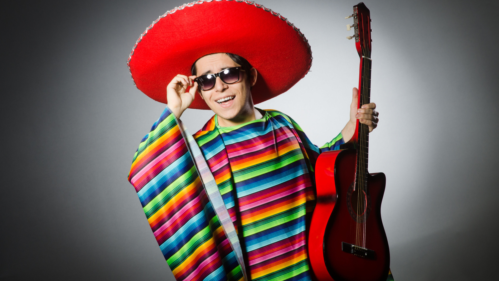 A man in a red sombrero with a guitar in his hands on a gray background