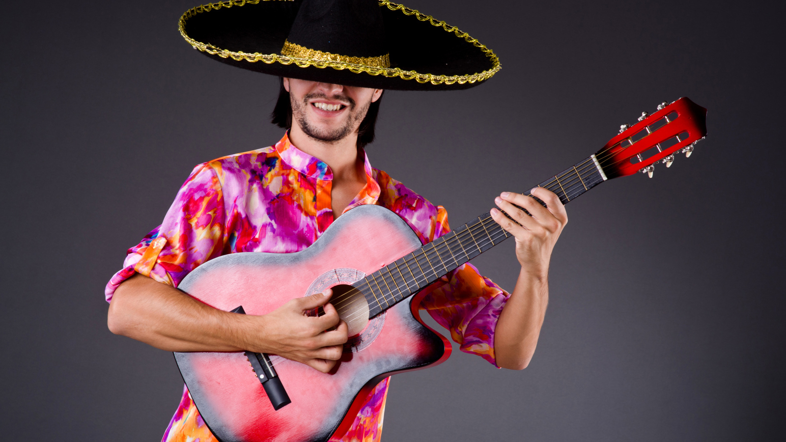 Мужчина в сомбреро с гитарой в руках на сером фоне
