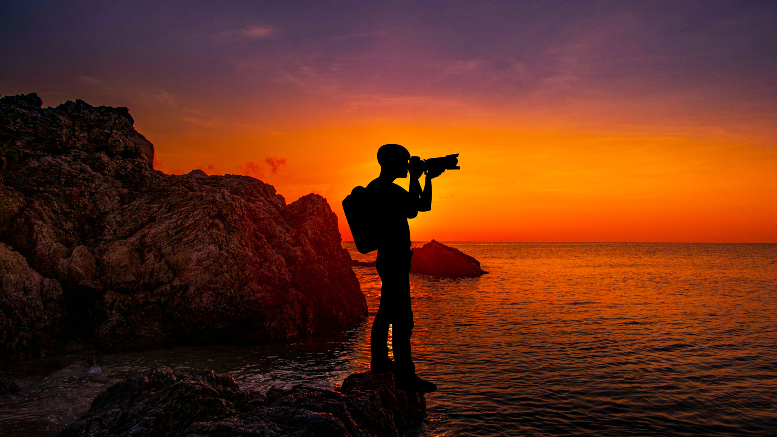 A man photographs a sunset by the sea