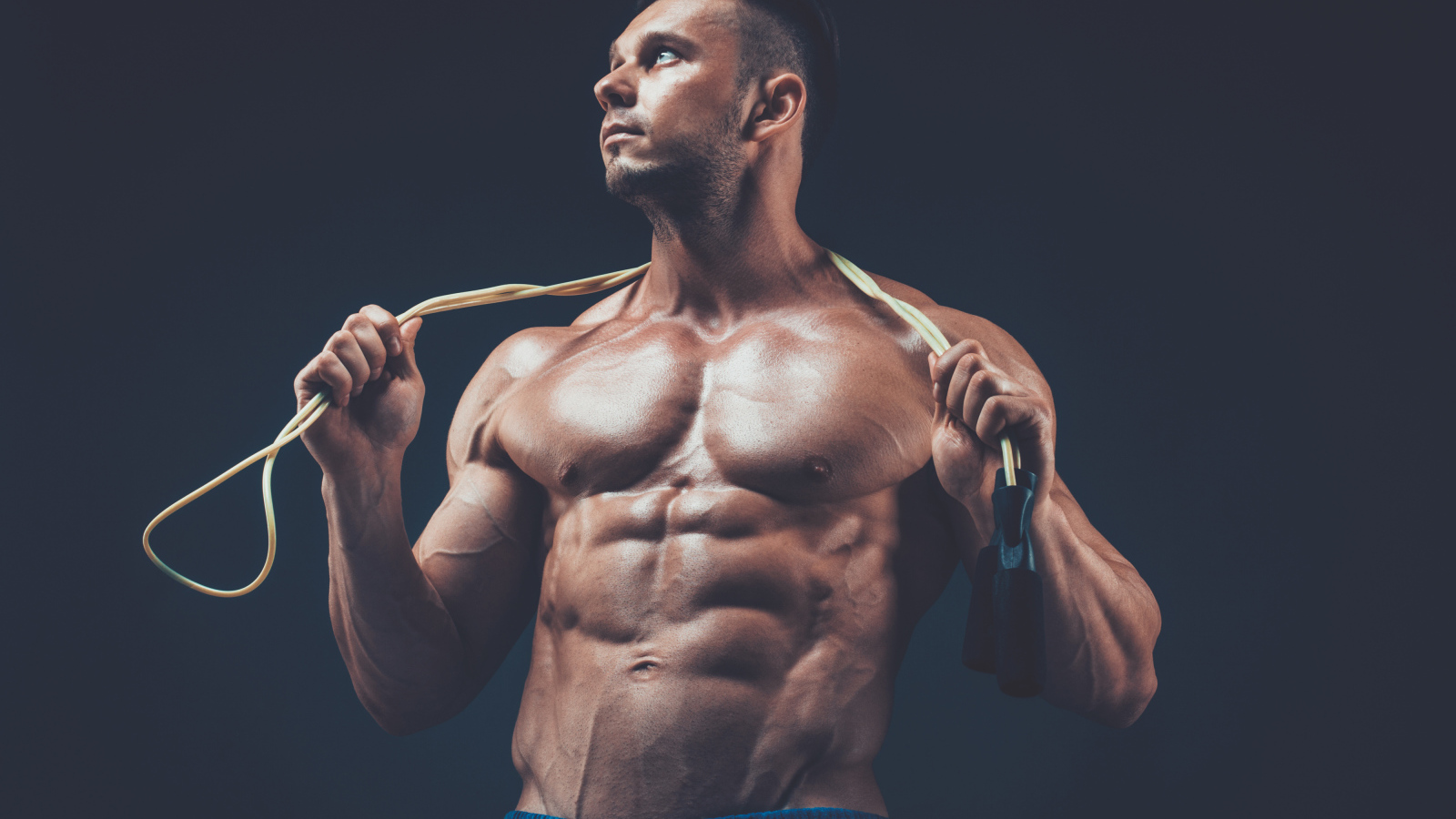 Накаченный мужчина со скакалкой в руках на сером фоне