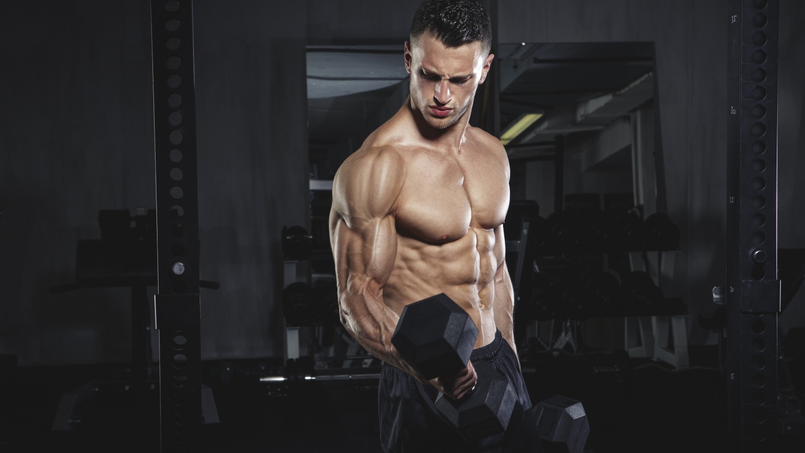 Накаченный мужчина с тяжелыми гантелями в руках 