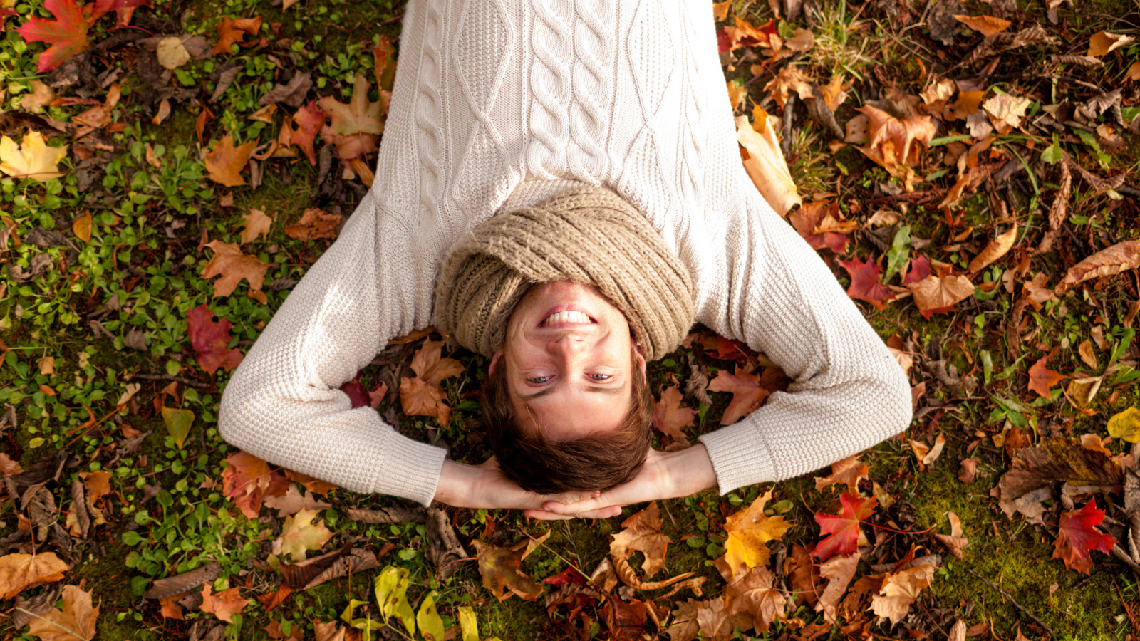 Улыбающийся мужчина в свитере лежит на опавших листьях 