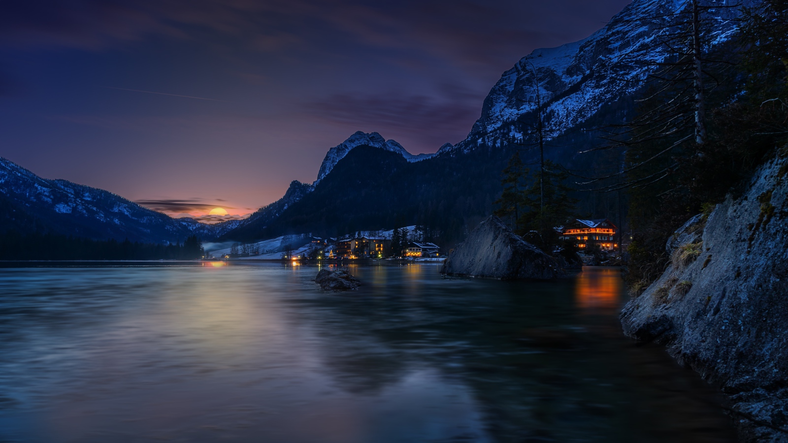 Город у озера на фоне заснеженных гор ночью 