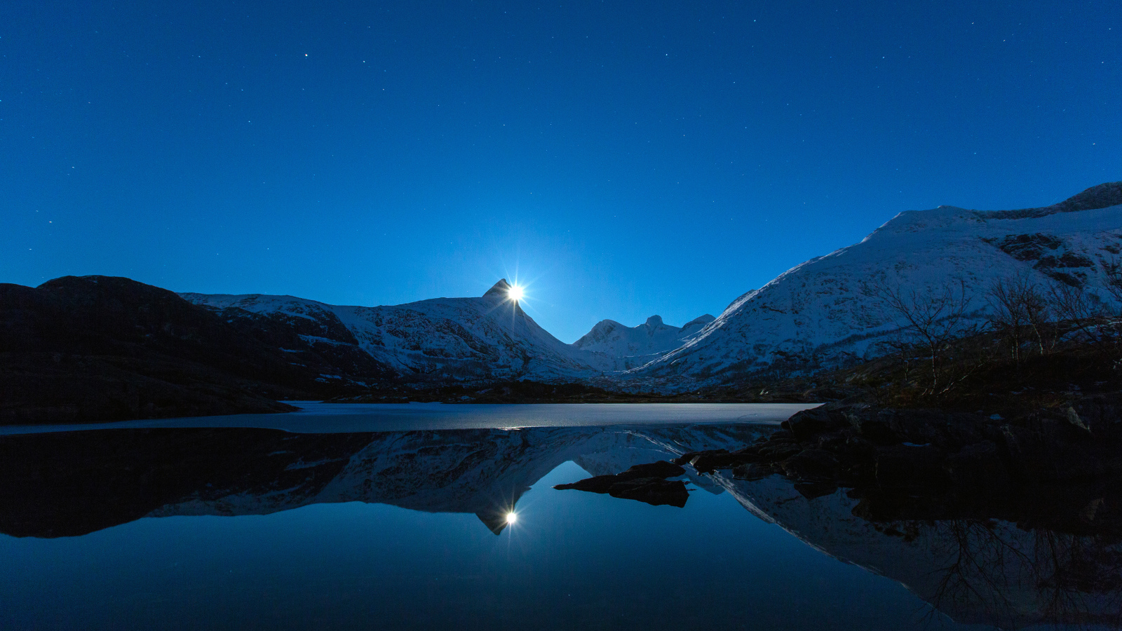 Луна и заснеженные горы отражаются в воде 