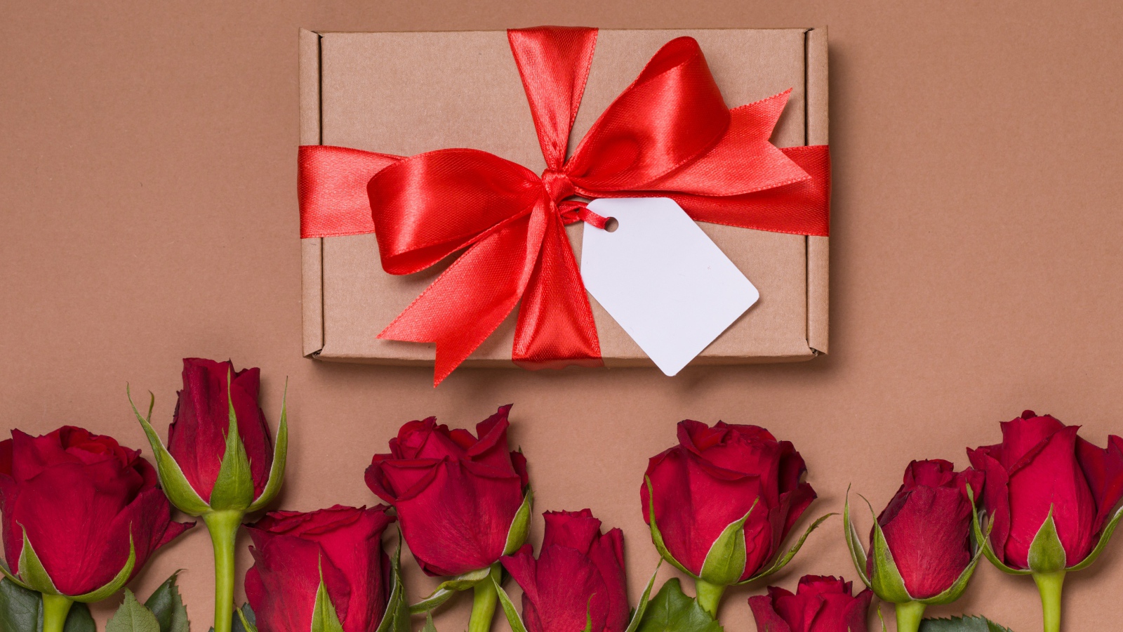 Подарок с красным бантом на бежевом фоне с красными розами