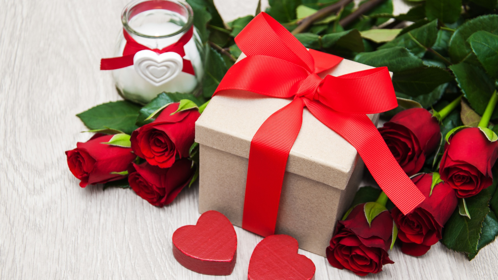 Красивый букет красных роз на столе со свечой и подарком