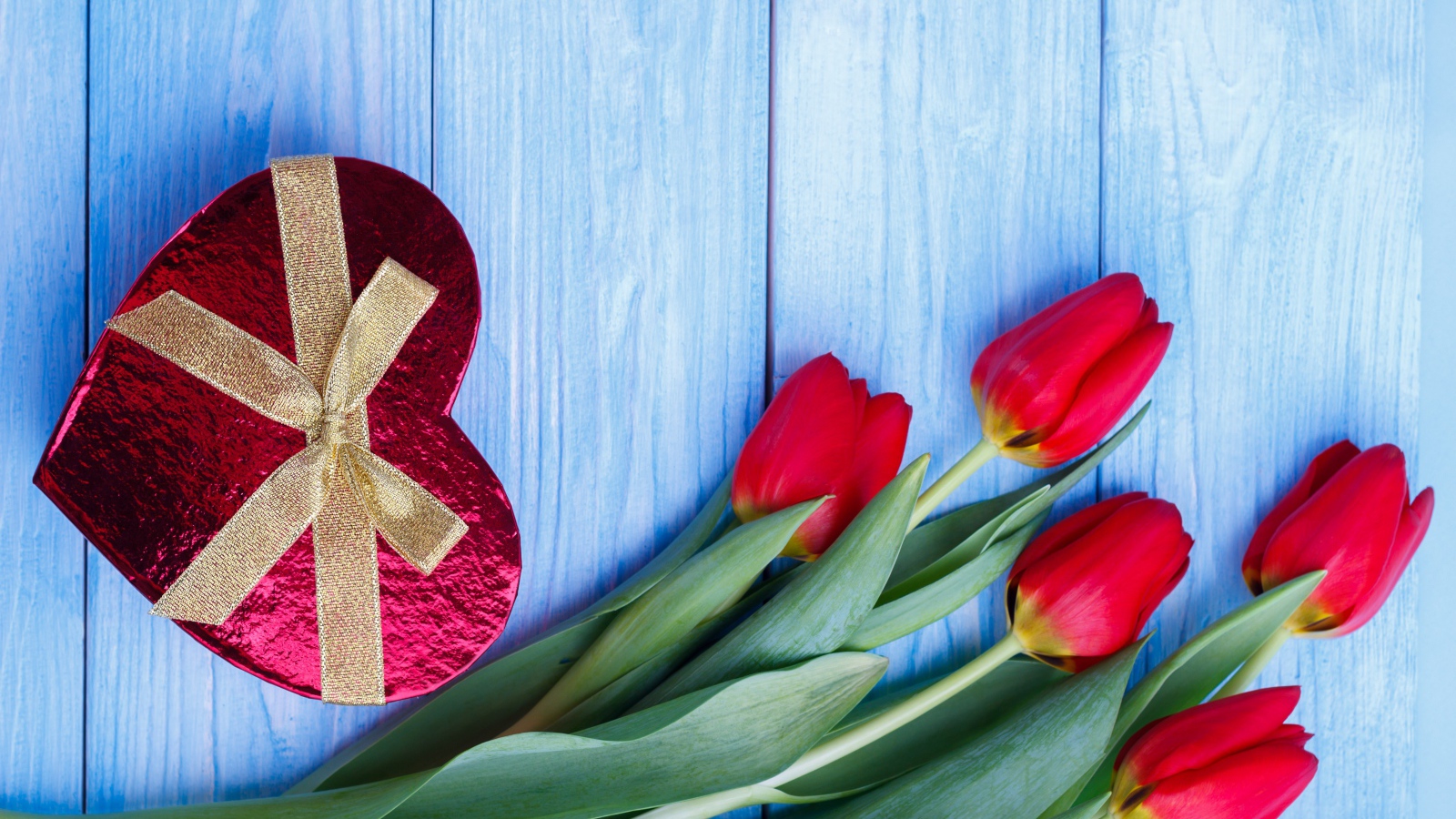 Букет красных тюльпанов на синем фоне с подарком в форме сердца