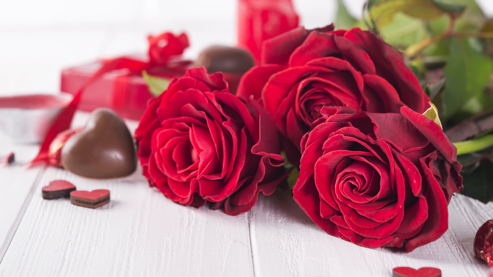 Три красивые красные розы на столе с конфетами