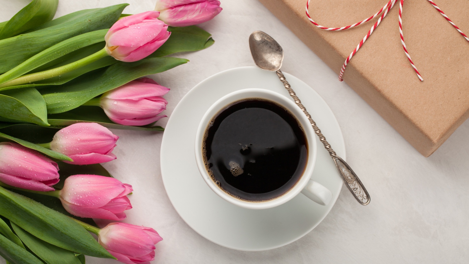 Белая чашка кофе на столе букетом розовых тюльпанов и подарком