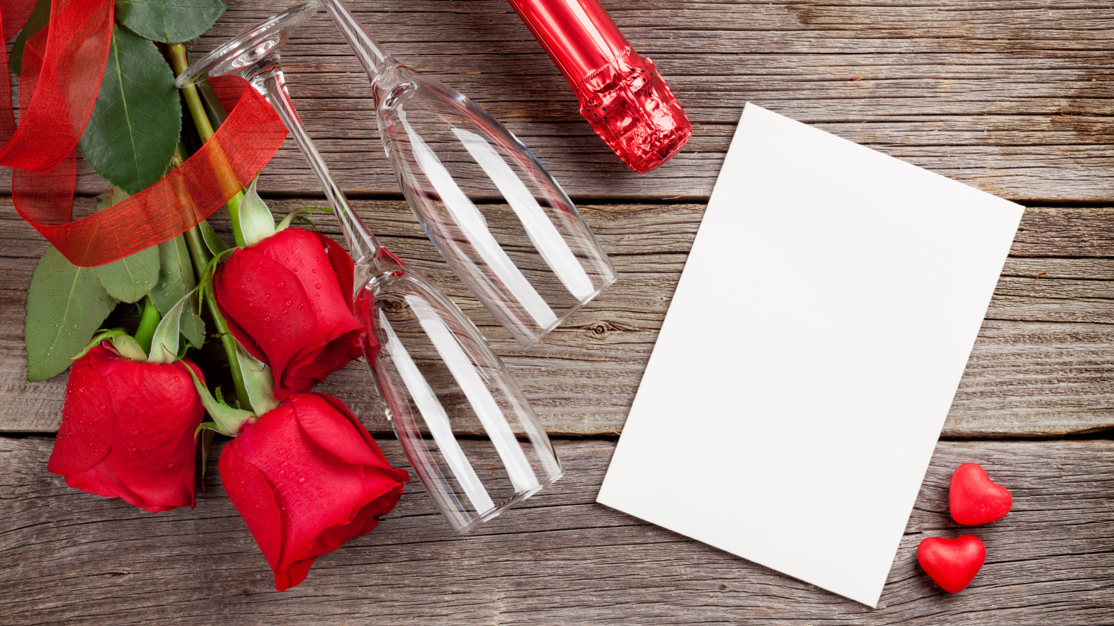 Белый лист бумаги на деревянном столе с бокалами и красными розами