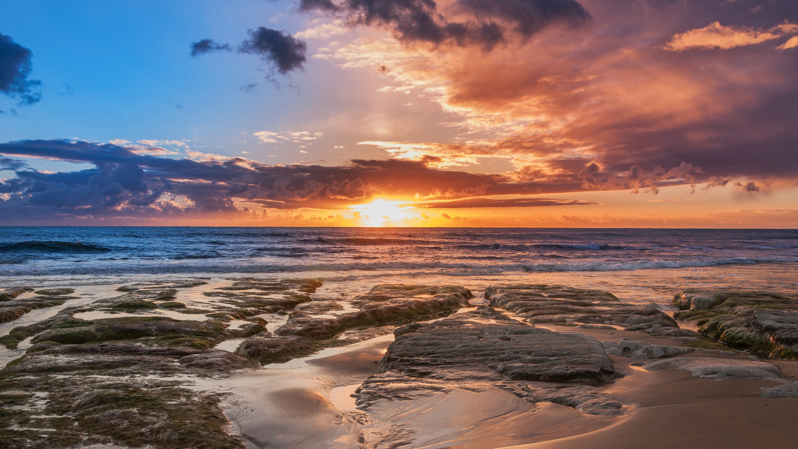 Мокрый песок и камни на берегу океана на закате солнца