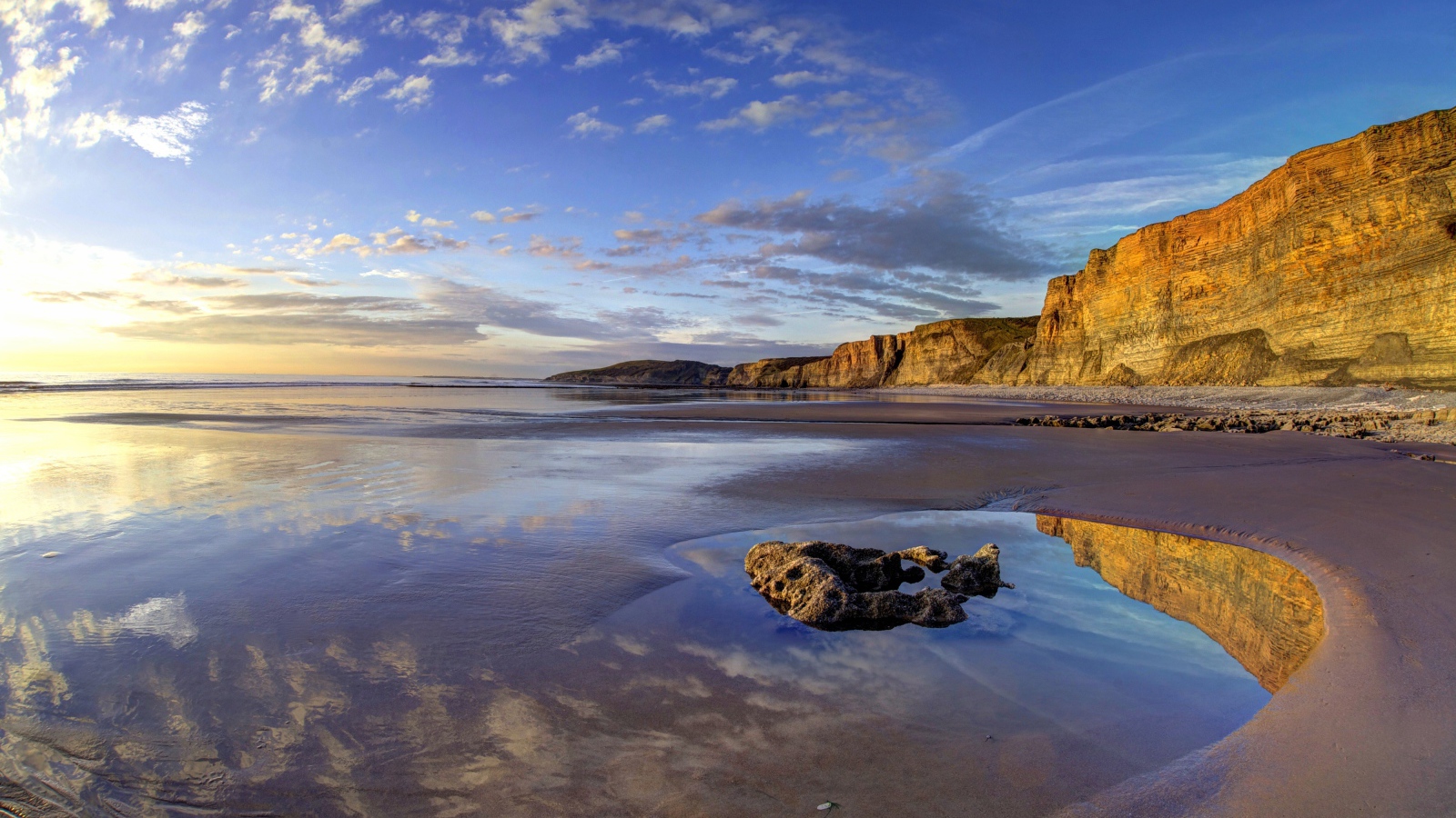 Мокрый морской берег со скалами на закате