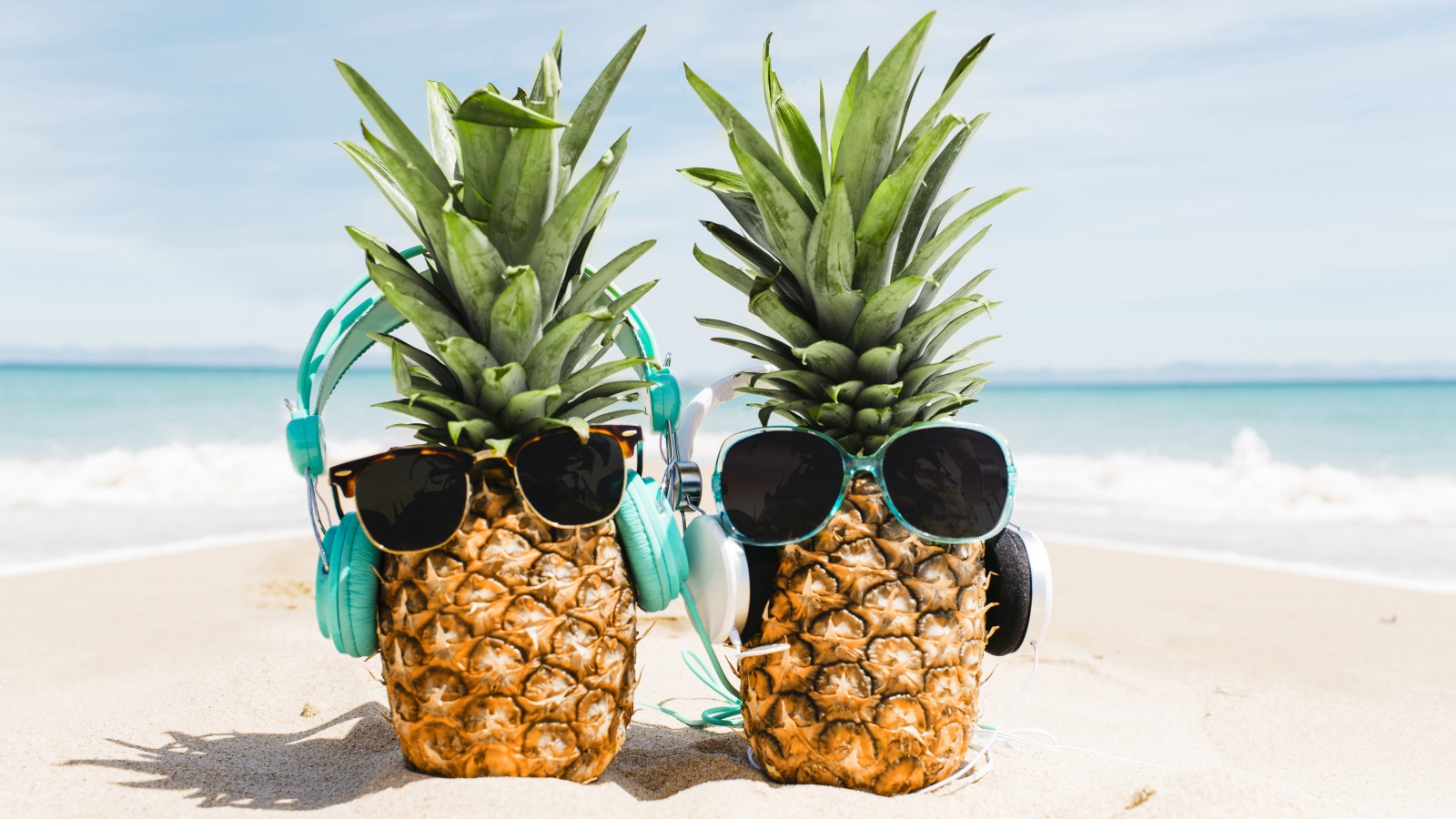 Два ананаса на пляже в солнечных очках и наушниках