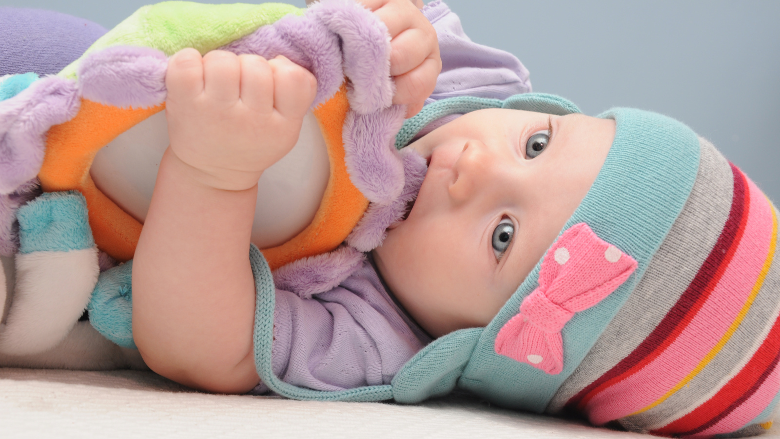 Младенец в шапке грызет мягкую игрушку