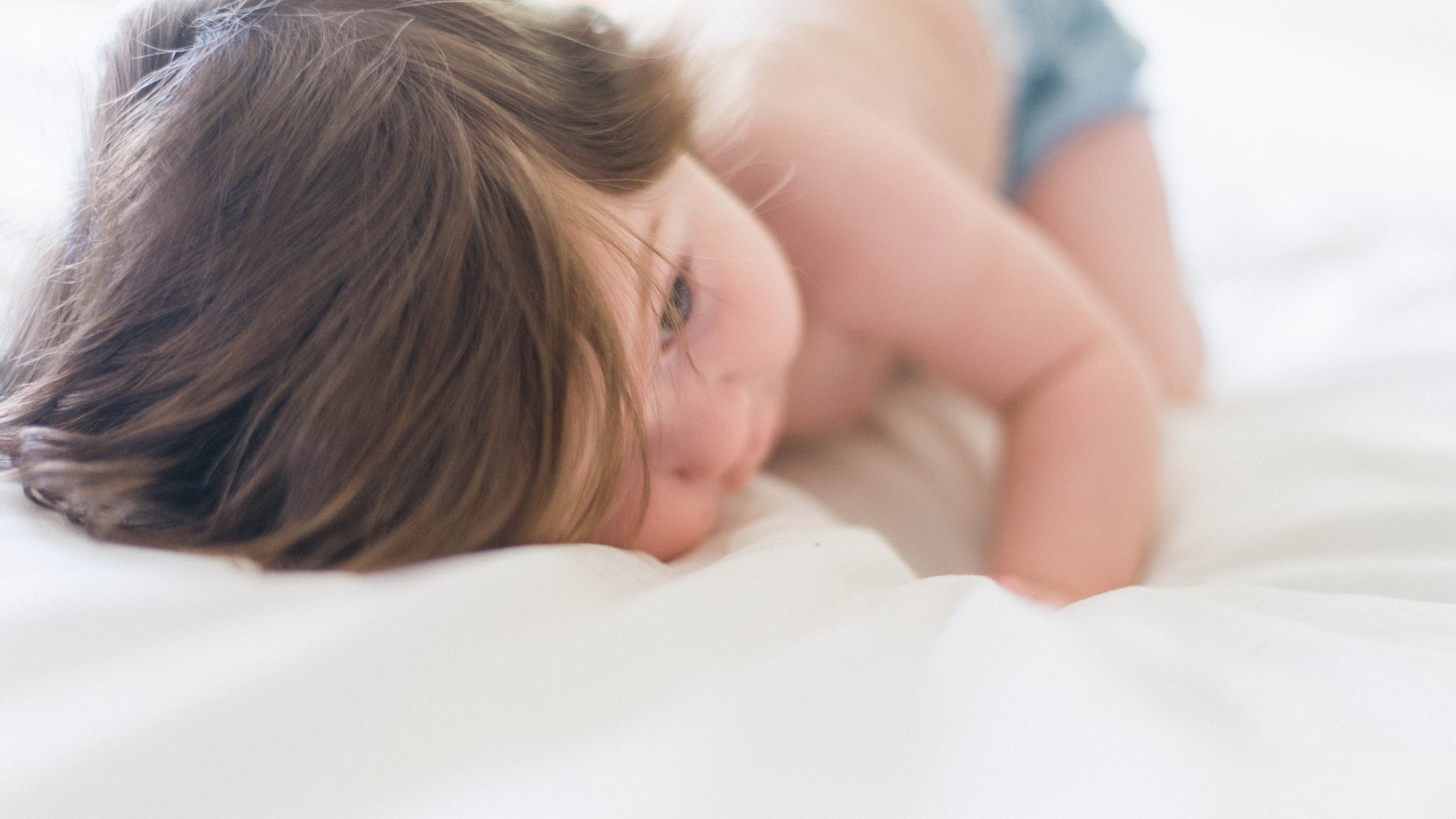 Маленький ребенок с русыми волосами лежит на кровати