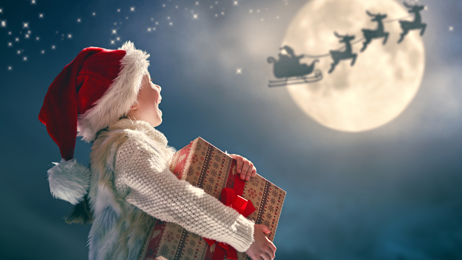 Маленький мальчик с подарком смотрит на улетающего Санта Клауса