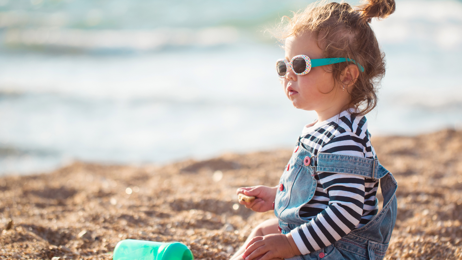 Маленькая девочка сидит на песке на пляже