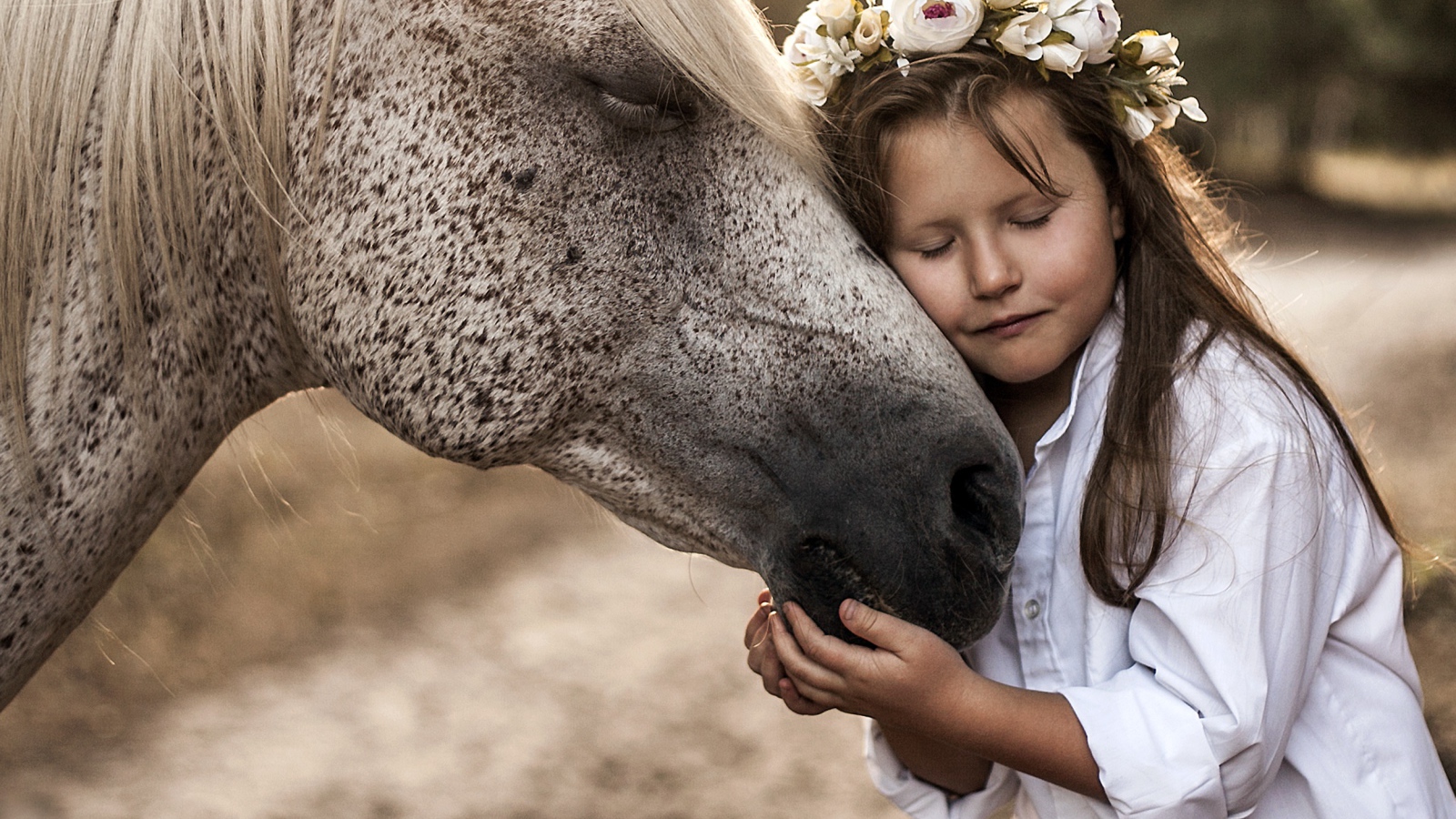 Маленькая девочка с венком на голове обнимает лошадь