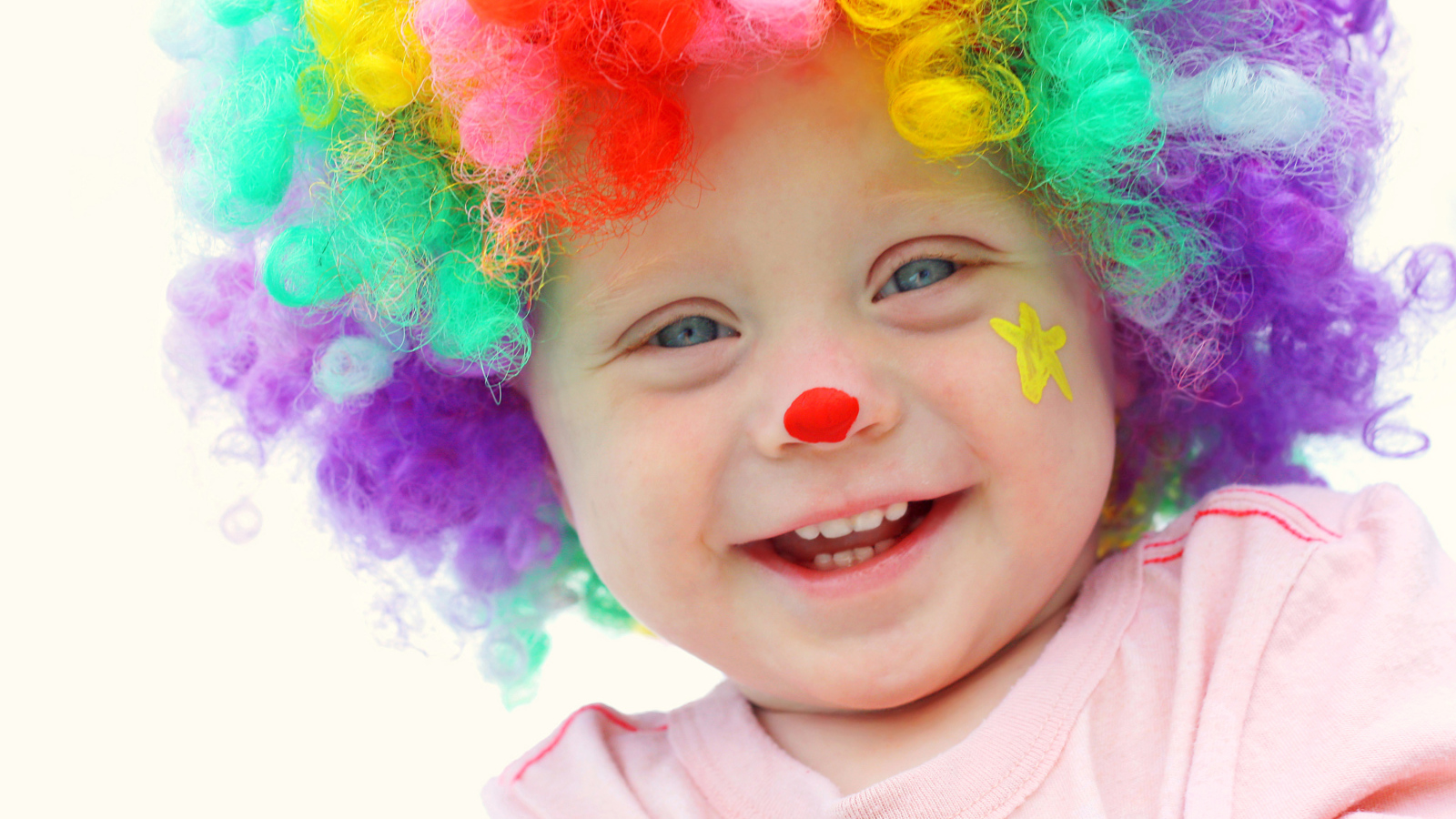 Маленький улыбающийся мальчик в костюме клоуна на белом фоне