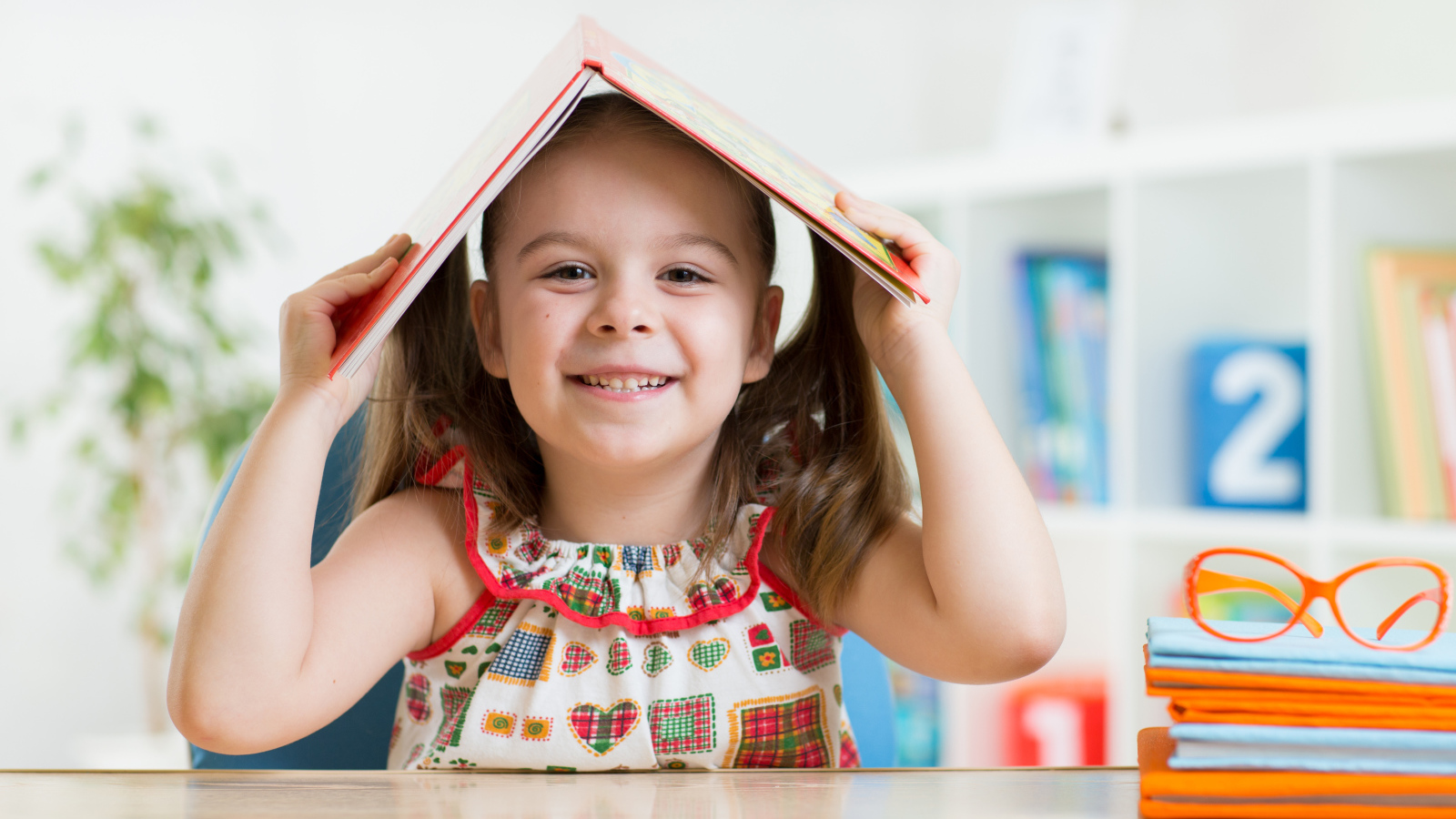 Маленькая улыбающаяся девочка с книгой на голове