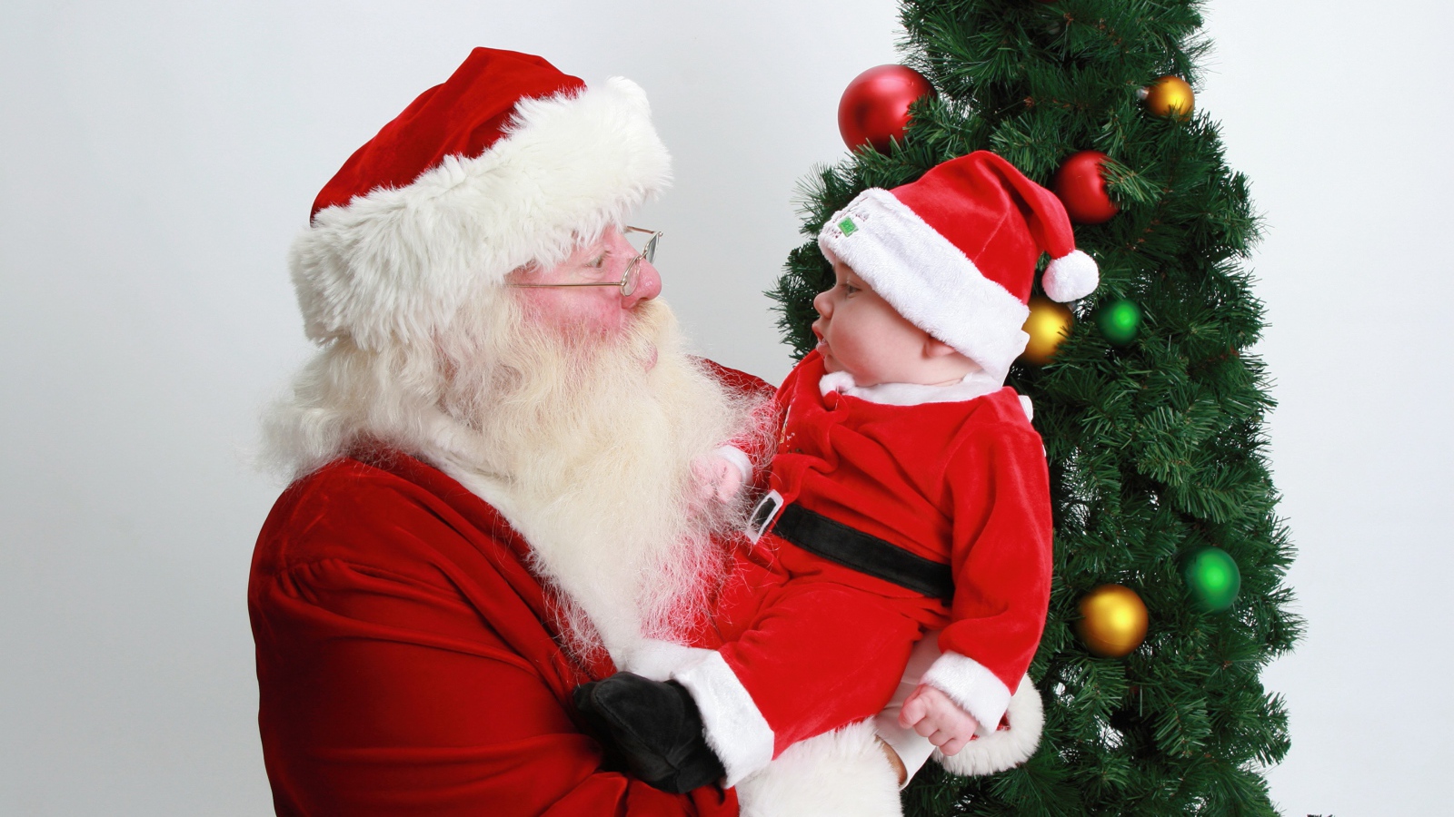 Дед Мороз держит на руках маленького ребенка у елки