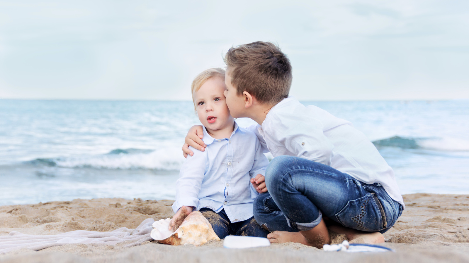 Два маленьких брата сидят на песке на пляже