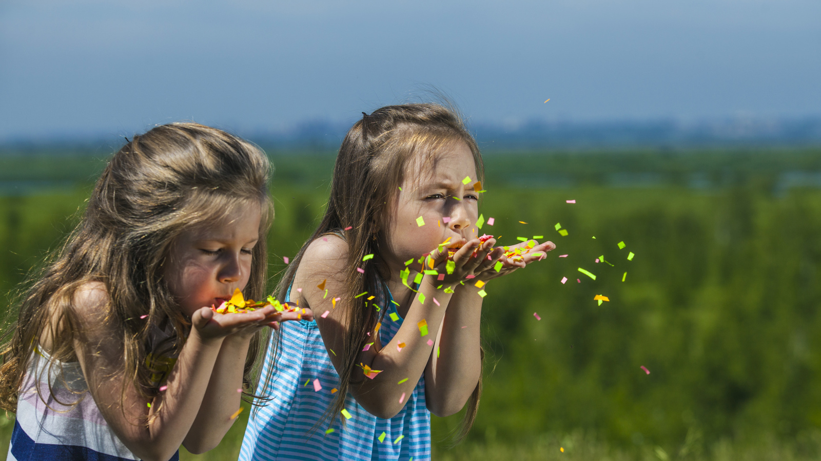 Две маленькие девочки сдувают конфетти  с рук