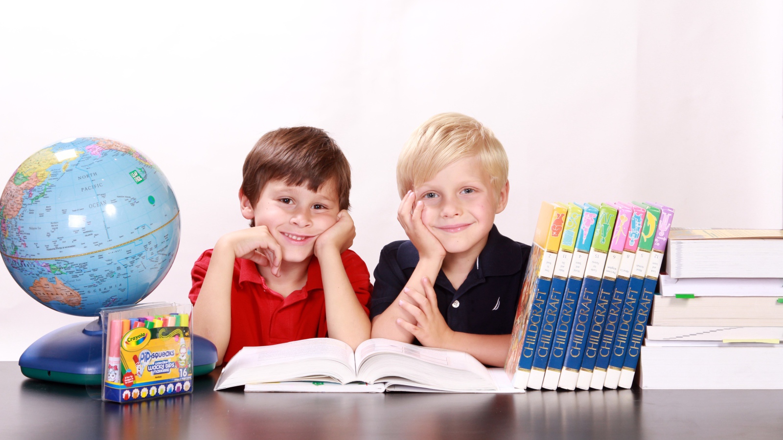 Два маленьких мальчика школьника за столом с книгами и глобусом