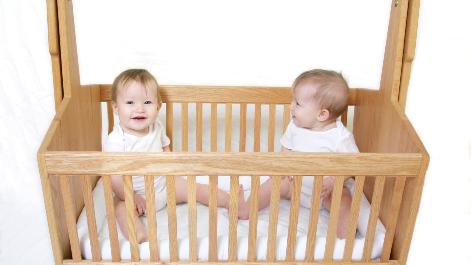 Два улыбающихся малыша в деревянной кроватке