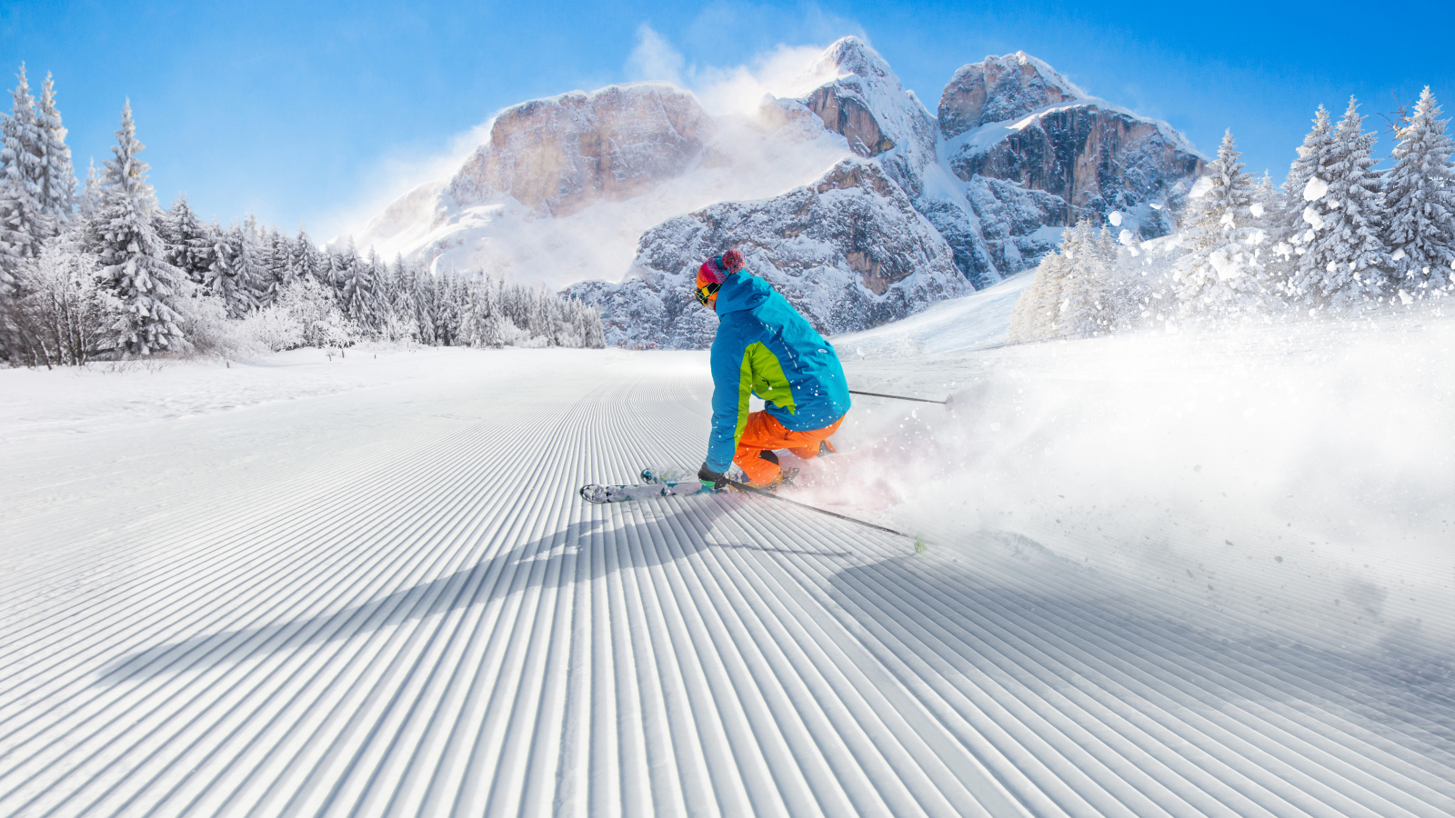 Лыжник спускается по склону на фоне заснеженных гор 