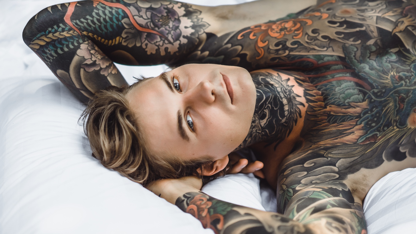 Красивый молодой человек с татуировками на теле лежит на кровати