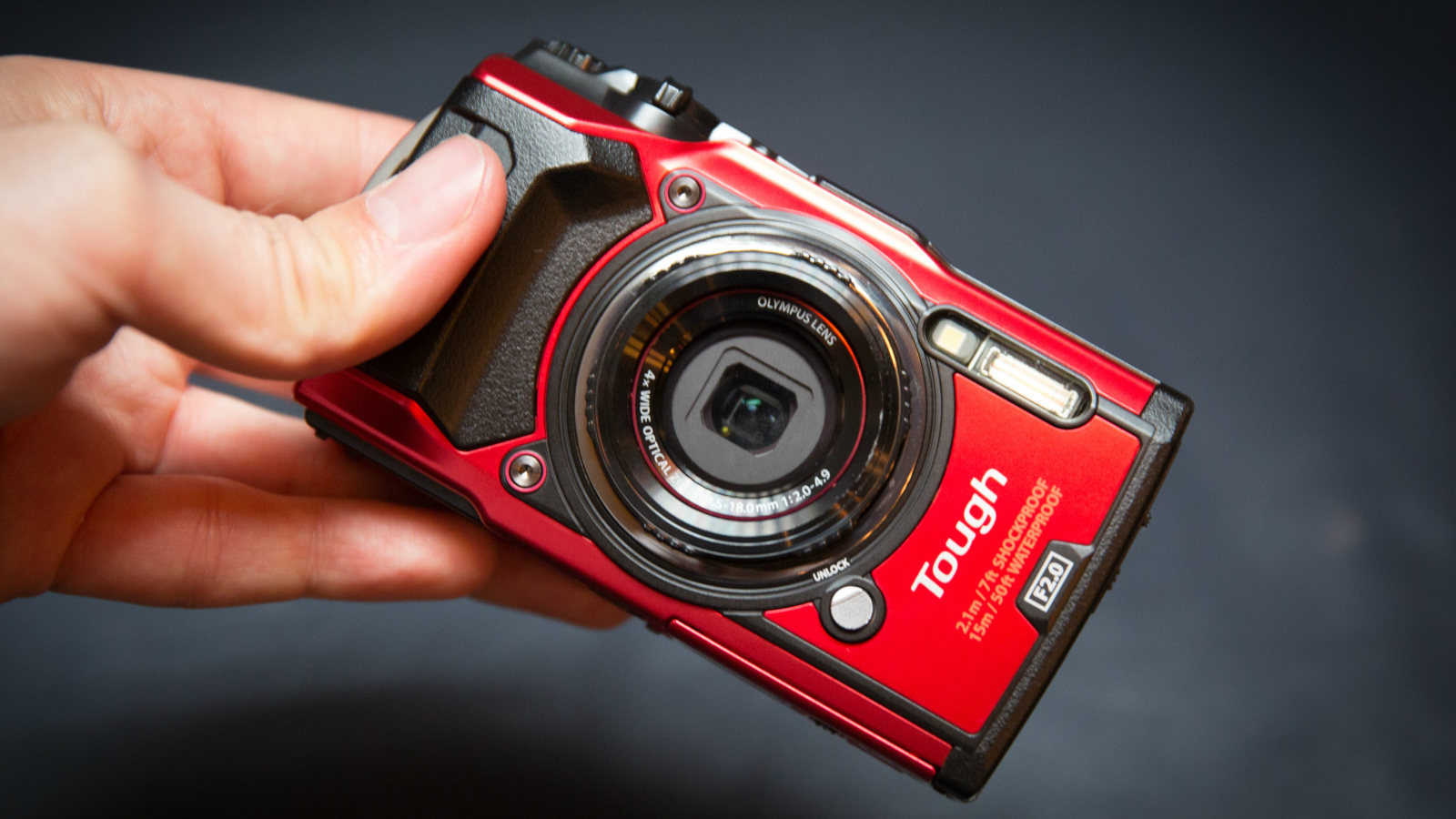 Красный фотоаппарат Olympus Tough TG-5 в руке на сером фоне