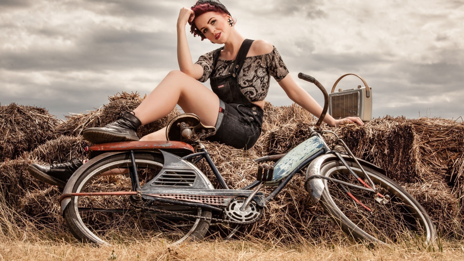 Retro girl sitting on a hay with a bicycle
