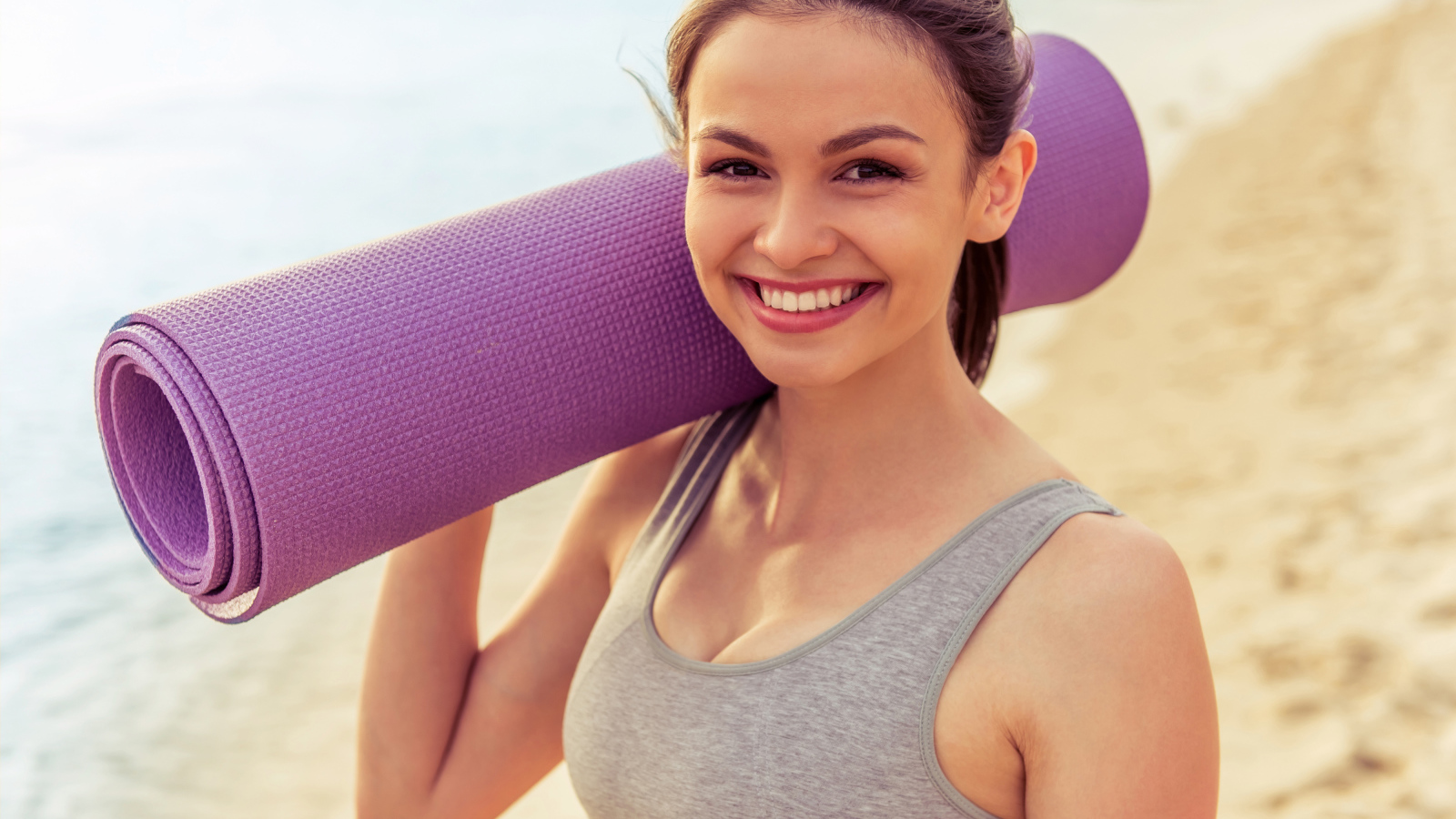Спортивная девушка с ковриком для йоги на пляже