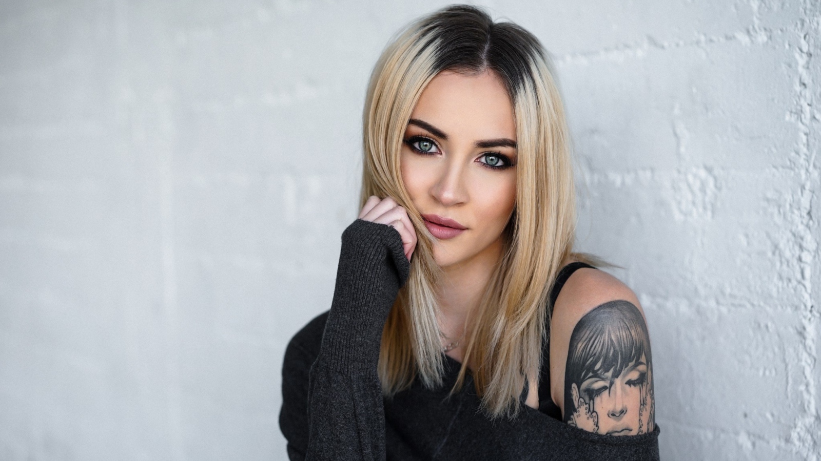 Стильная блондинка с татуировкой на плече на фоне стены