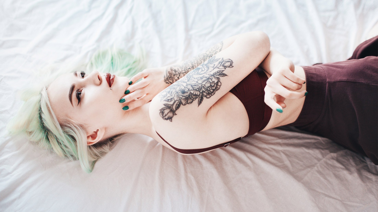Девушка с татуировкой на руке лежит на кровати 