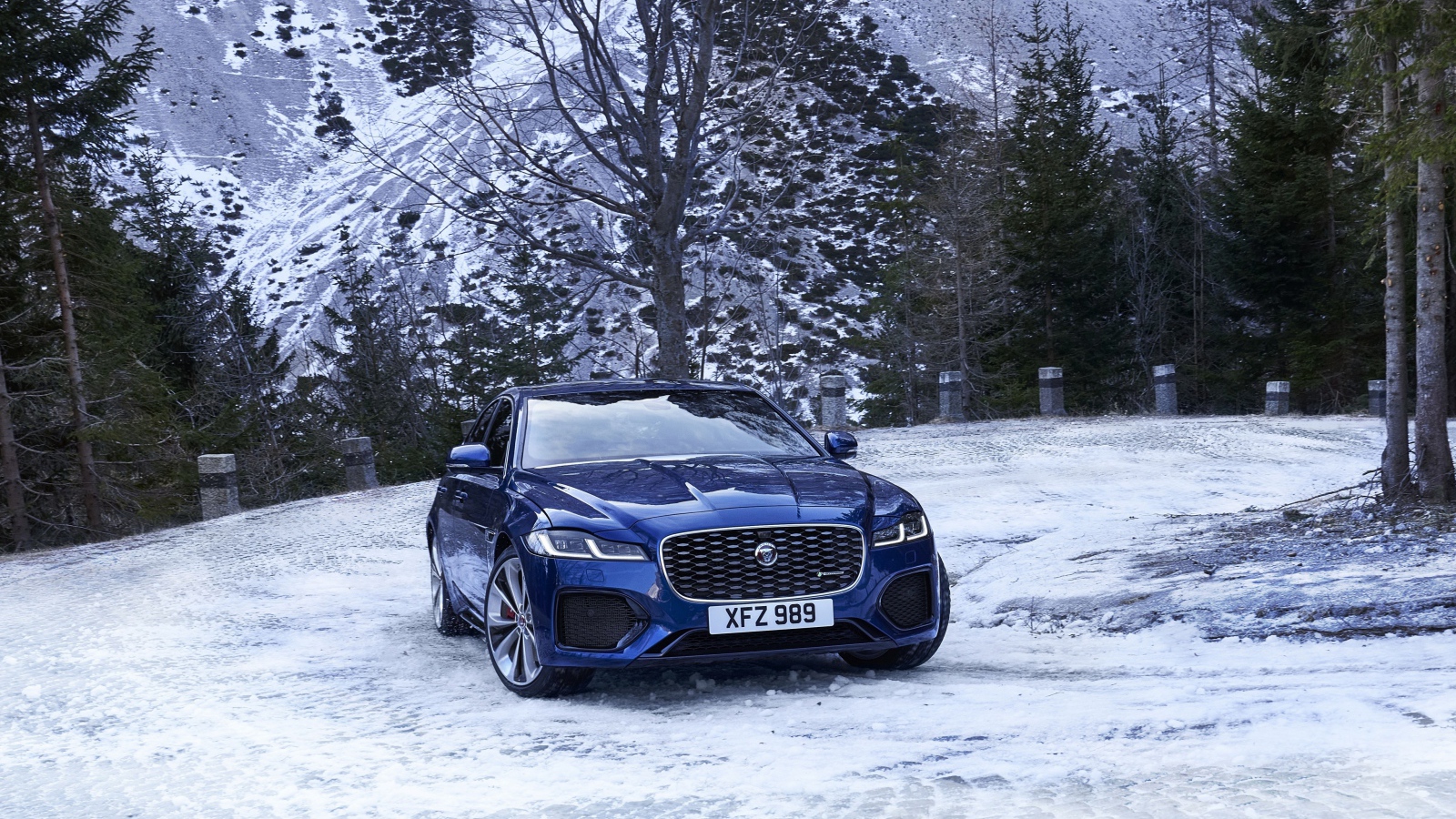 Синий автомобиль Jaguar XF зимой на фоне горы 