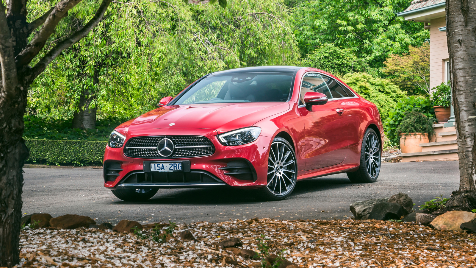 Красный автомобиль Mercedes-Benz E 300 AMG, 2020 года у дома осенью