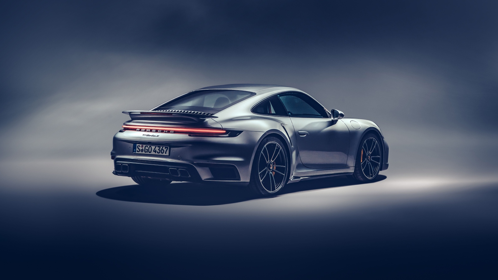 Автомобиль Porsche 911 Turbo S 2020 года на сером фоне вид сзади
