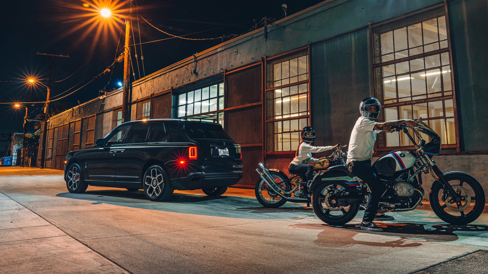 Черный автомобиль Rolls-Royce Cullinan, 2020 года у гаража с байкерами